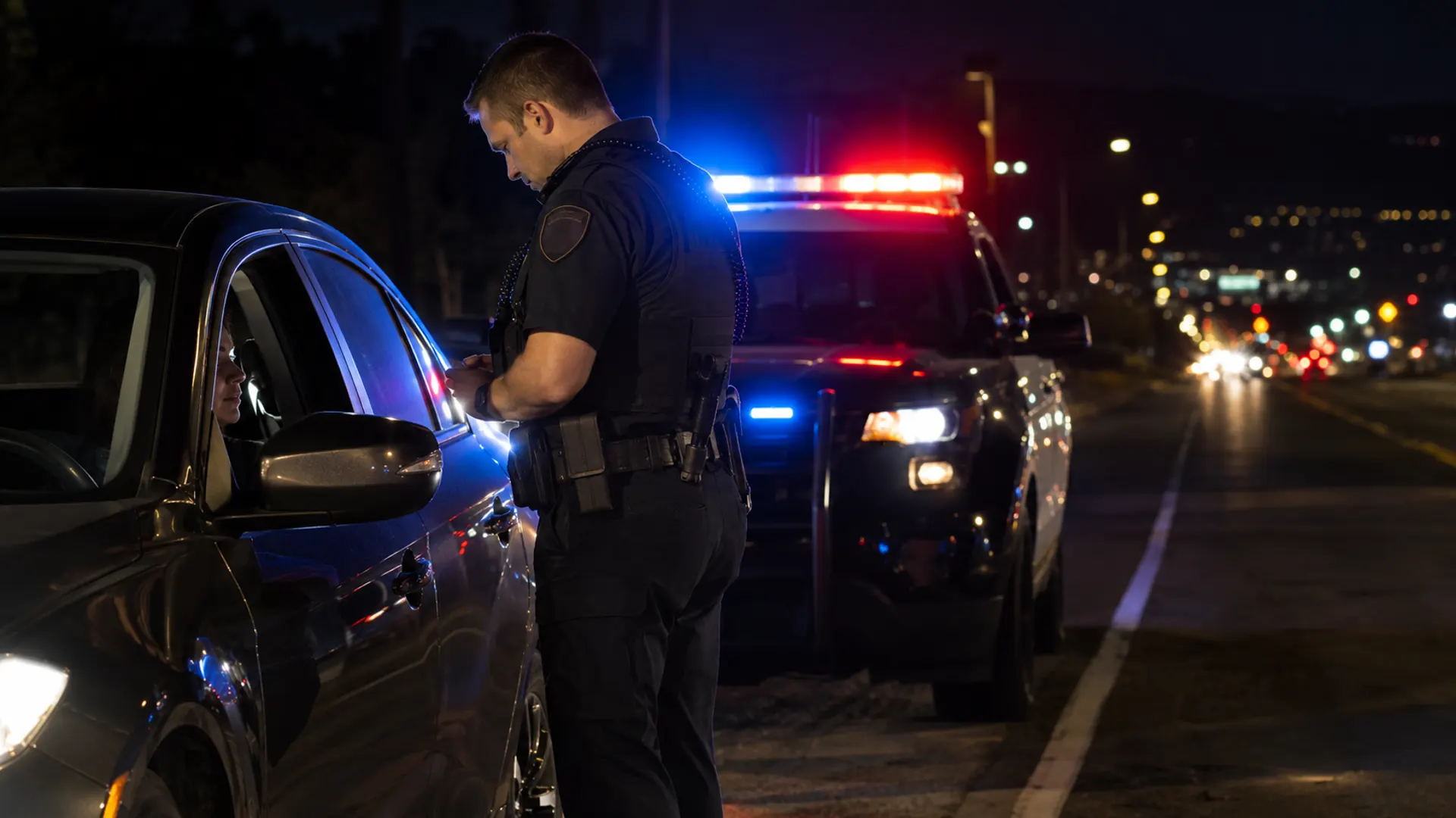 A police officer at a nighttime traffic stop, speaking with a driver